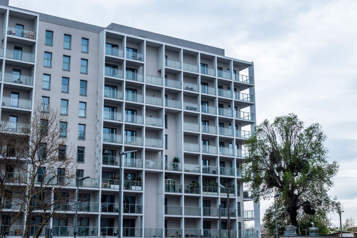 A tall apartment building with balconies beside green trees