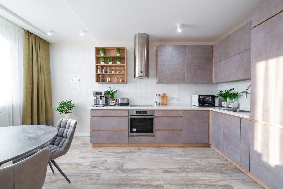 A modern kitchen with grey cabinets, a built-in oven and a dining table