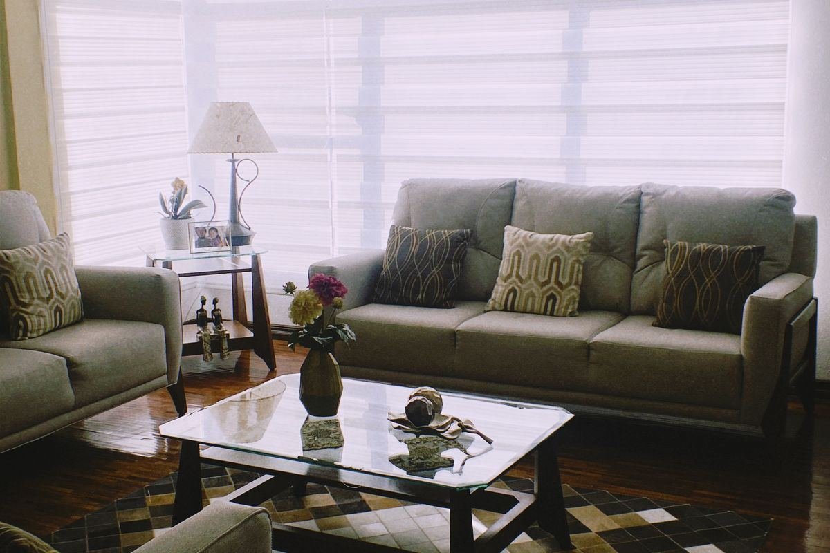 A living room with green sofas, a glass coffee table and a lamp by the window